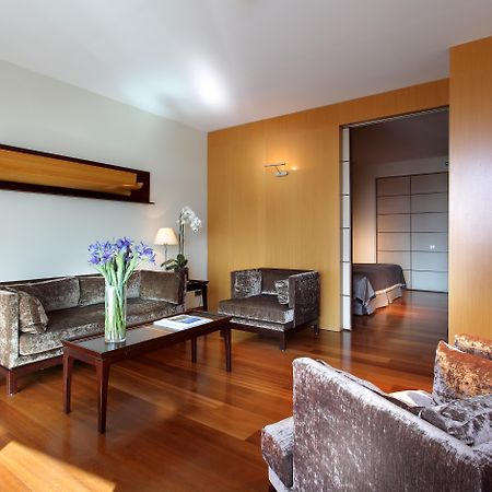 Eurostars Grand Marina Hotel Gl Barcelona Exterior photo The photo shows a modern living room with a warm and inviting atmosphere. It features two armchairs and a sofa, all in a plush, dark fabric. A coffee table sits in the center, with a vase of fresh flowers adding a pop of color. The room has hardwood 