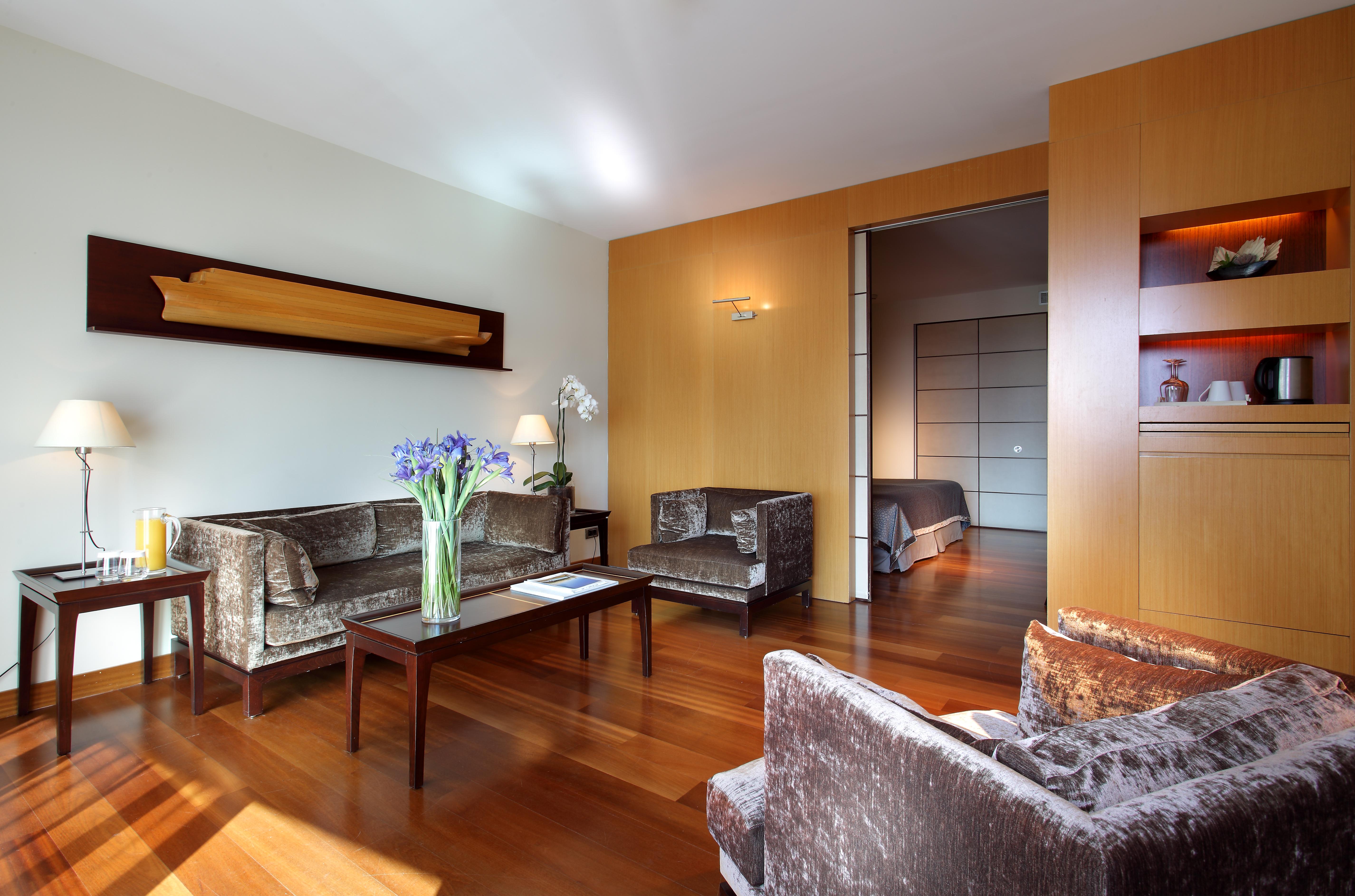 Eurostars Grand Marina Hotel Gl Barcelona Exterior photo The photo shows a modern living room with a warm and inviting atmosphere. It features two armchairs and a sofa, all in a plush, dark fabric. A coffee table sits in the center, with a vase of fresh flowers adding a pop of color. The room has hardwood 