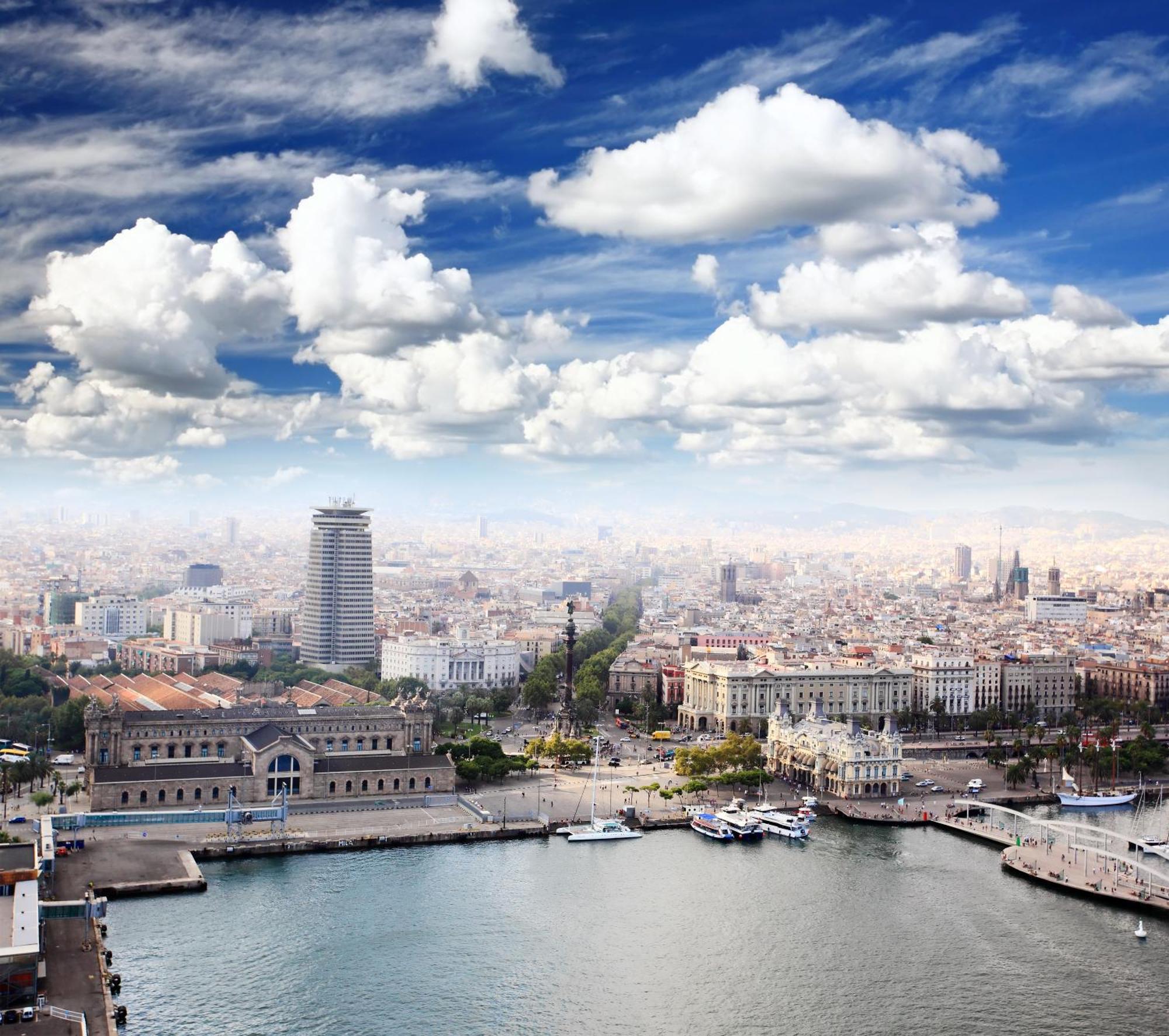 Eurostars Grand Marina Hotel Gl Barcelona Exterior photo The image shows a panoramic view of a cityscape, likely featuring a coastal area with a harbor. In the foreground, there are buildings near the water, including a large structure that might be a historic or notable building. The scene extends into th