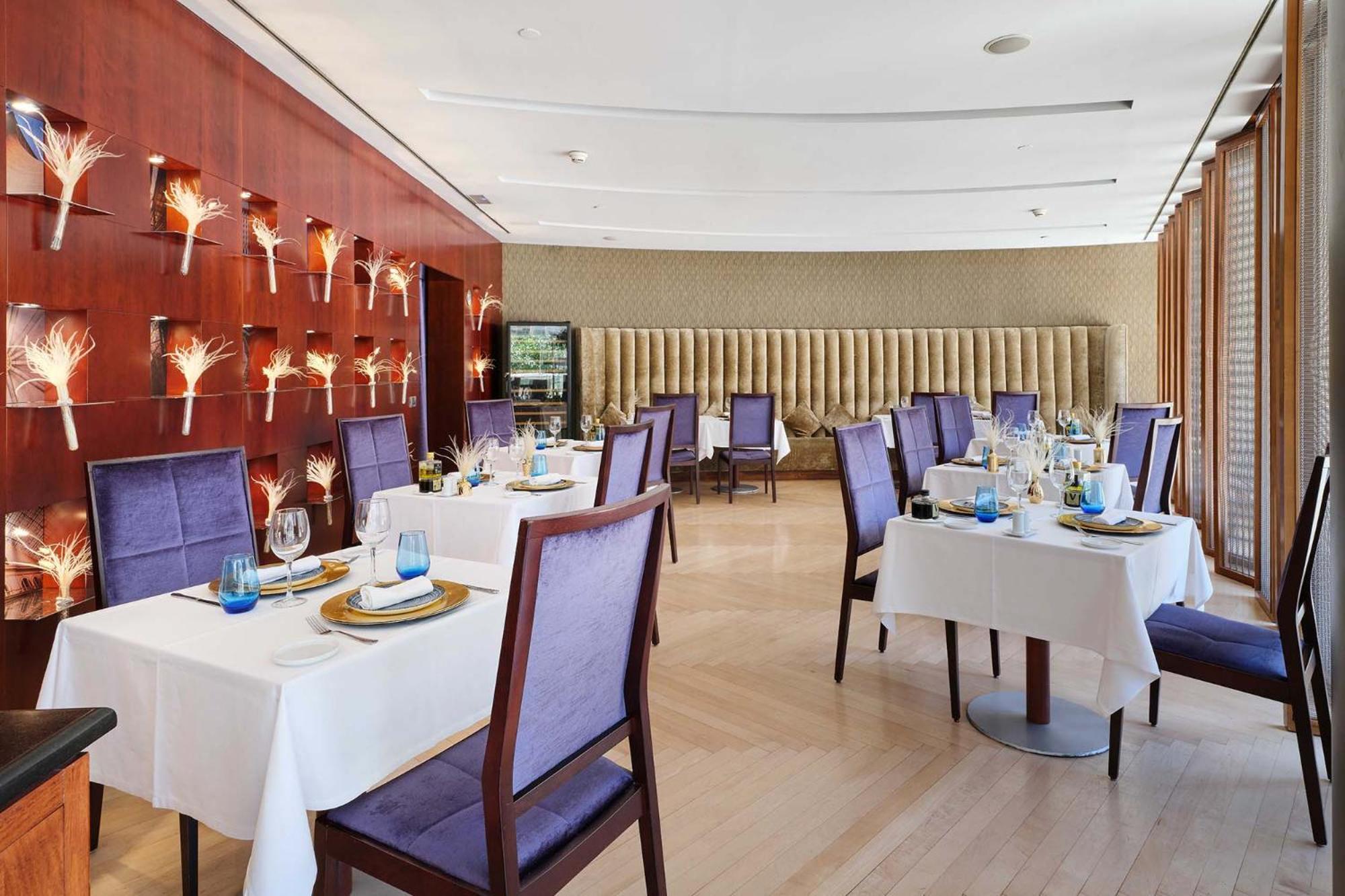 Eurostars Grand Marina Hotel Gl Barcelona Exterior photo The photo shows an elegant dining room in a restaurant. There are several tables set with white tablecloths, each adorned with plates, glasses, and decorative items. The chairs have a purple upholstery, adding a touch of color to the space. 

The wal